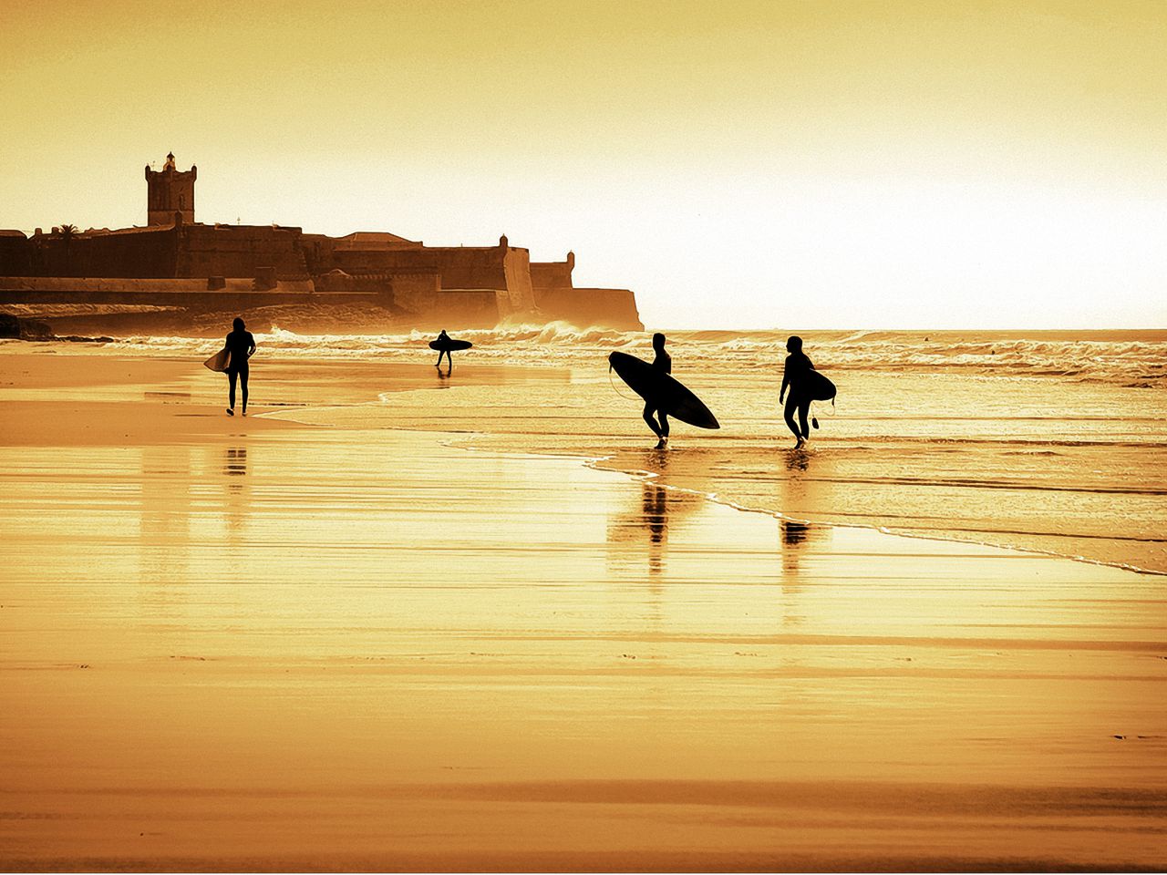 Surfers at sunset at Carcavelos Beach with the St. Julian de Barra fortress in the background
